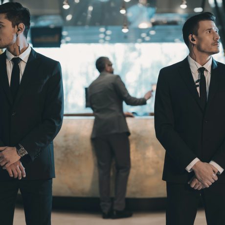 two-bodyguards-waiting-for-businessman-standing-at-reception-counter.jpg